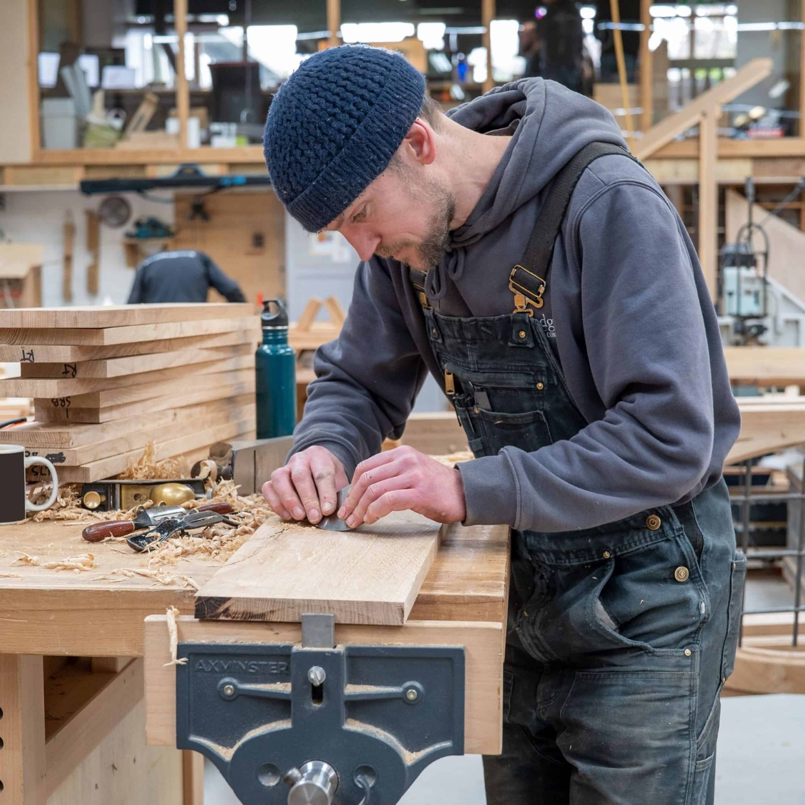 Woodworker Steve Brown concentrates on refining a pile of oak planks at a workbench. Steve learned his woodworking skills at the Boat Building Academy.